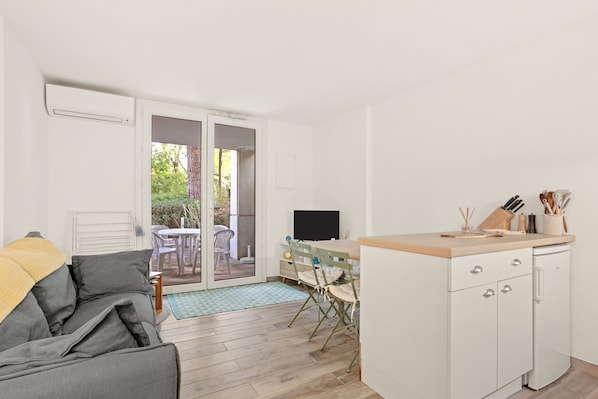 A compact living space with a sofa, a dining area with a table and chairs, a kitchen with a counter and cabinets, and a sliding glass door leading to an outdoor area.