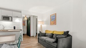 Un espacio habitable moderno con cocina, un sofá gris y una manta amarilla, y una lámpara.