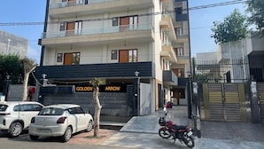 A multi-story residential building with a gated entrance, parked cars, and a motorcycle. - Hotel Golden Arrow (Noida)