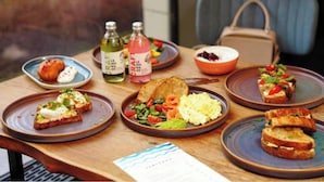 A table with various dishes including toast, scrambled eggs, and a salad, along with two bottles of drinks. - Hotel Golden Arrow (Noida)