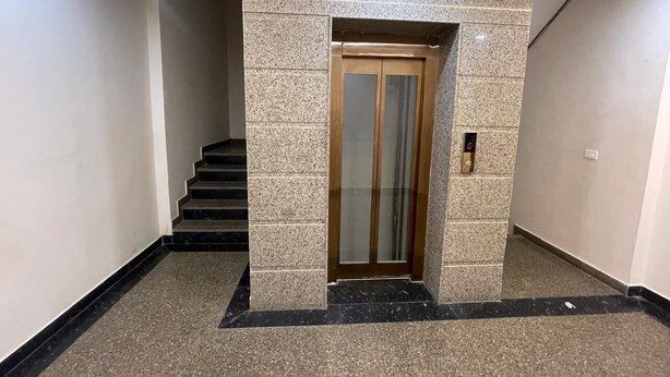 A hallway with a marble floor, a staircase, and a wooden elevator door. - Hotel Golden Arrow (Noida)
