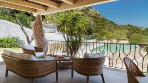A patio with wicker furniture, a stone pillar, and a view of a pool and mountains. - Villa 'Amata' with Sea View, Wi-Fi and Air Conditioning (Arzachena)
