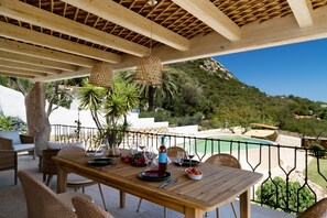 An outdoor dining area with a wooden table and wicker chairs, overlooking a pool and greenery. - Villa 'Amata' with Sea View, Wi-Fi and Air Conditioning (Arzachena)