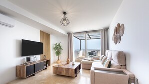 Una sala de estar moderna con un televisor de pantalla plana, una mesa de centro de madera, un sofá color crema y un ventanal con vistas.