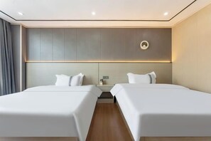 Une chambre d’hôtel moderne avec deux lits, une palette de couleurs neutres et un éclairage encastré au plafond.