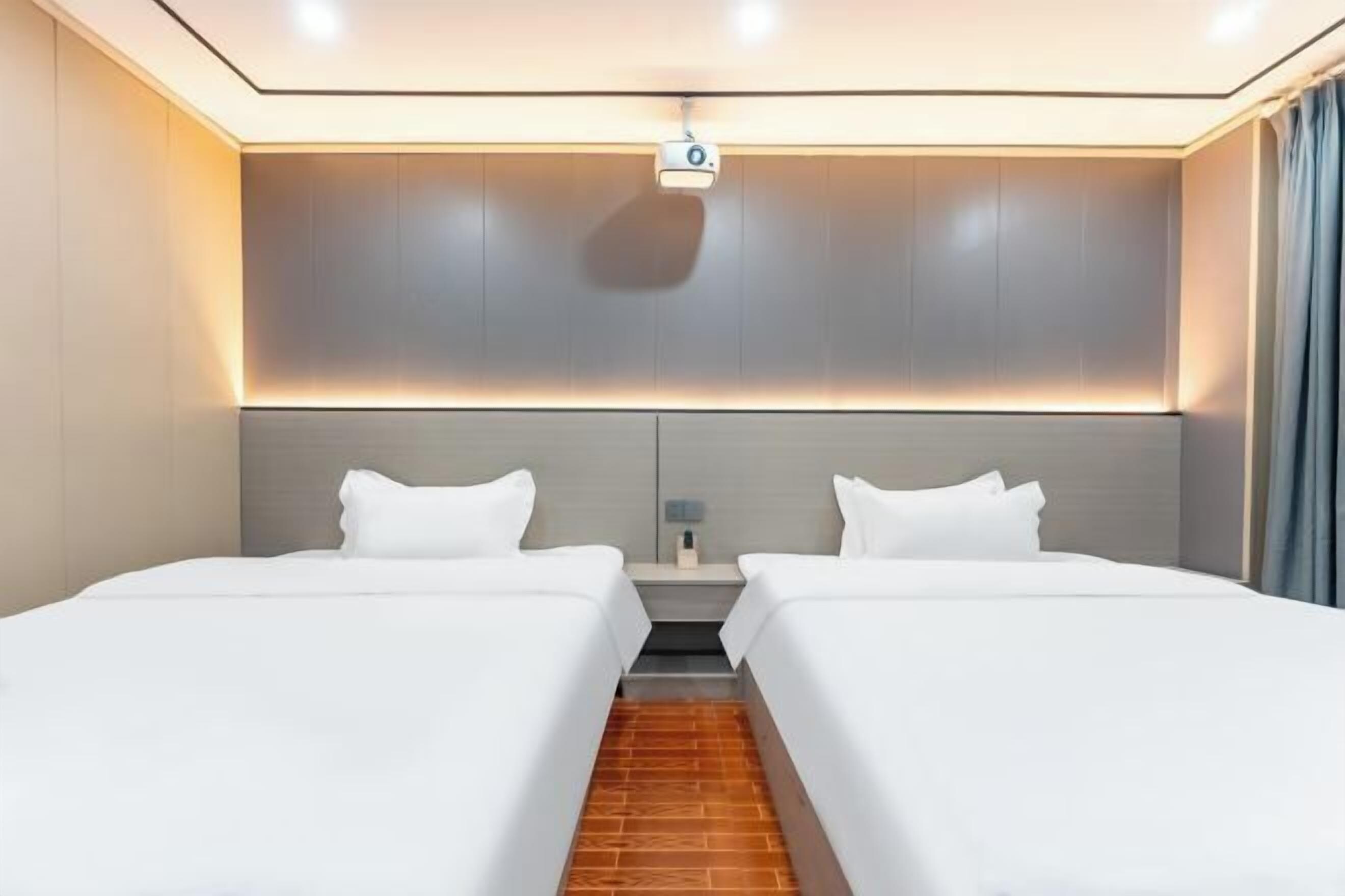 Ein modernes Hotelzimmer mit zwei Betten, einem Nachttisch, einem Projektor und Holzboden.