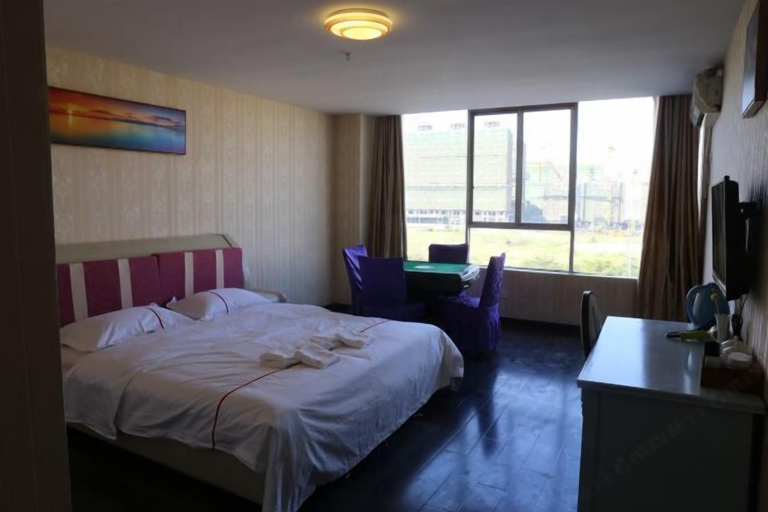 Habitación de hotel con cama, escritorio, silla y un ventanal con vistas a un edificio.
