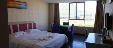 Habitación de hotel con cama, escritorio, silla y un ventanal con vistas a un edificio.