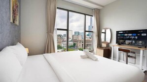 A hotel room with a large bed, a desk with a computer, a TV, and a window with a city view.