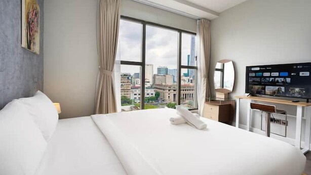 A hotel room with a large bed, a desk with a computer, a TV, and a window with a city view. - Saigon Royal - Trendy Modern Apartment (Ho Chi Minh City)