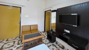 Habitación de hotel con sofá, una mesita, televisor montado en la pared y ventilador de techo.