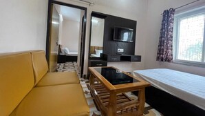 Una habitación de hotel compacta con sofá, una pequeña mesa de madera, cama, televisor montado en la pared y ventana con cortinas.