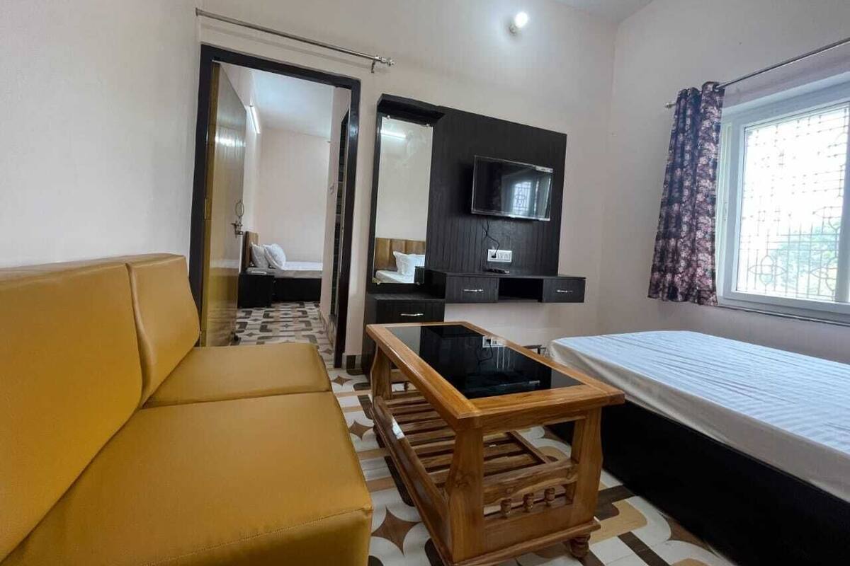 Une chambre d’hôtel compacte comprenant un canapé, une petite table en bois, un lit, un téléviseur fixé au mur et une fenêtre avec des rideaux.
