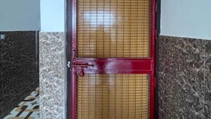Una puerta con marco rojo y diseño de cuadrícula, frente a una pared con estampado similar al mármol.