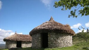 Two stone huts with thatched roofs on a grassy hill.