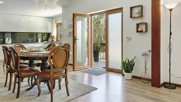 A dining area with a round table, chairs, a chandelier, and a view through glass doors to an outdoor area.