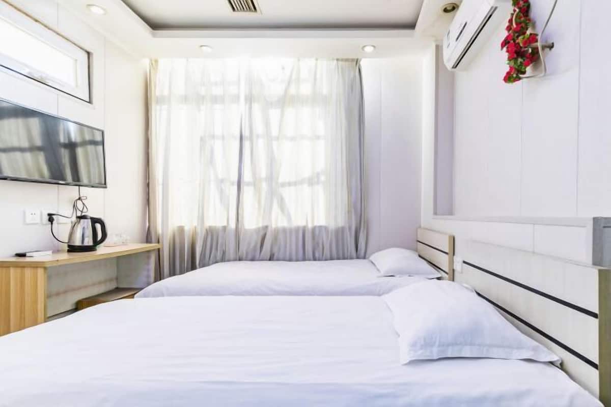Habitación de hotel con dos camas, televisión, hervidor de agua y ventana con cortinas traslúcidas.