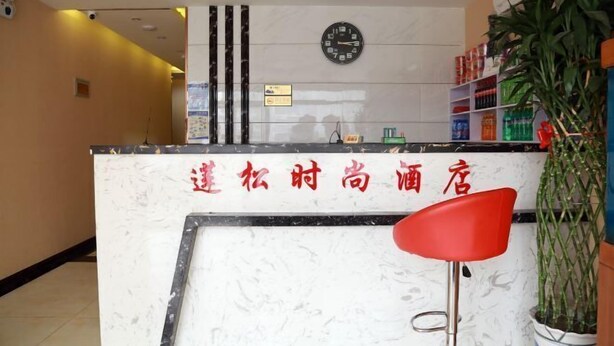 Zona de recepción de un hotel con un mostrador de mármol, un reloj y una silla roja.