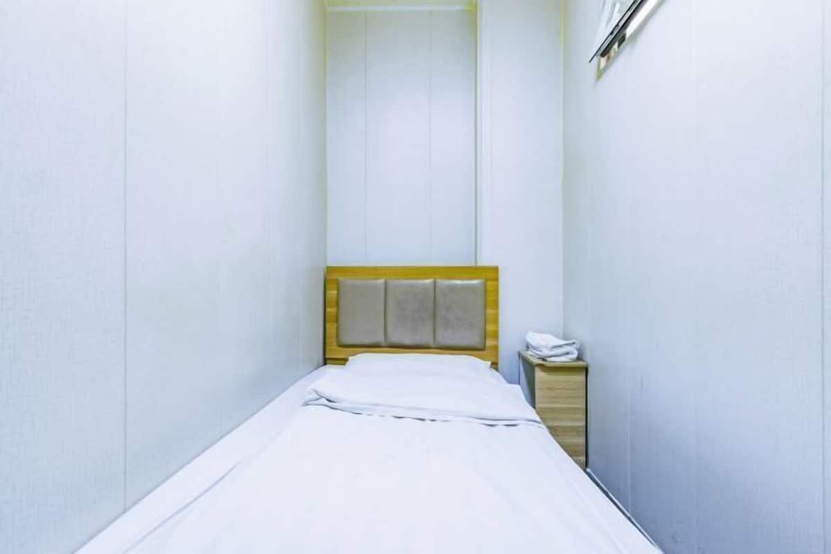 Una habitación pequeña con cama individual, cabecera de madera, mesita de noche y teléfono en la pared.