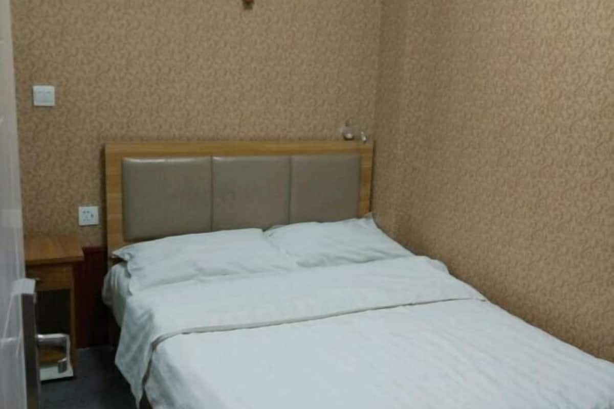 Una habitación pequeña con cama individual, cabecera de madera, mesita de noche y enchufe en la pared.