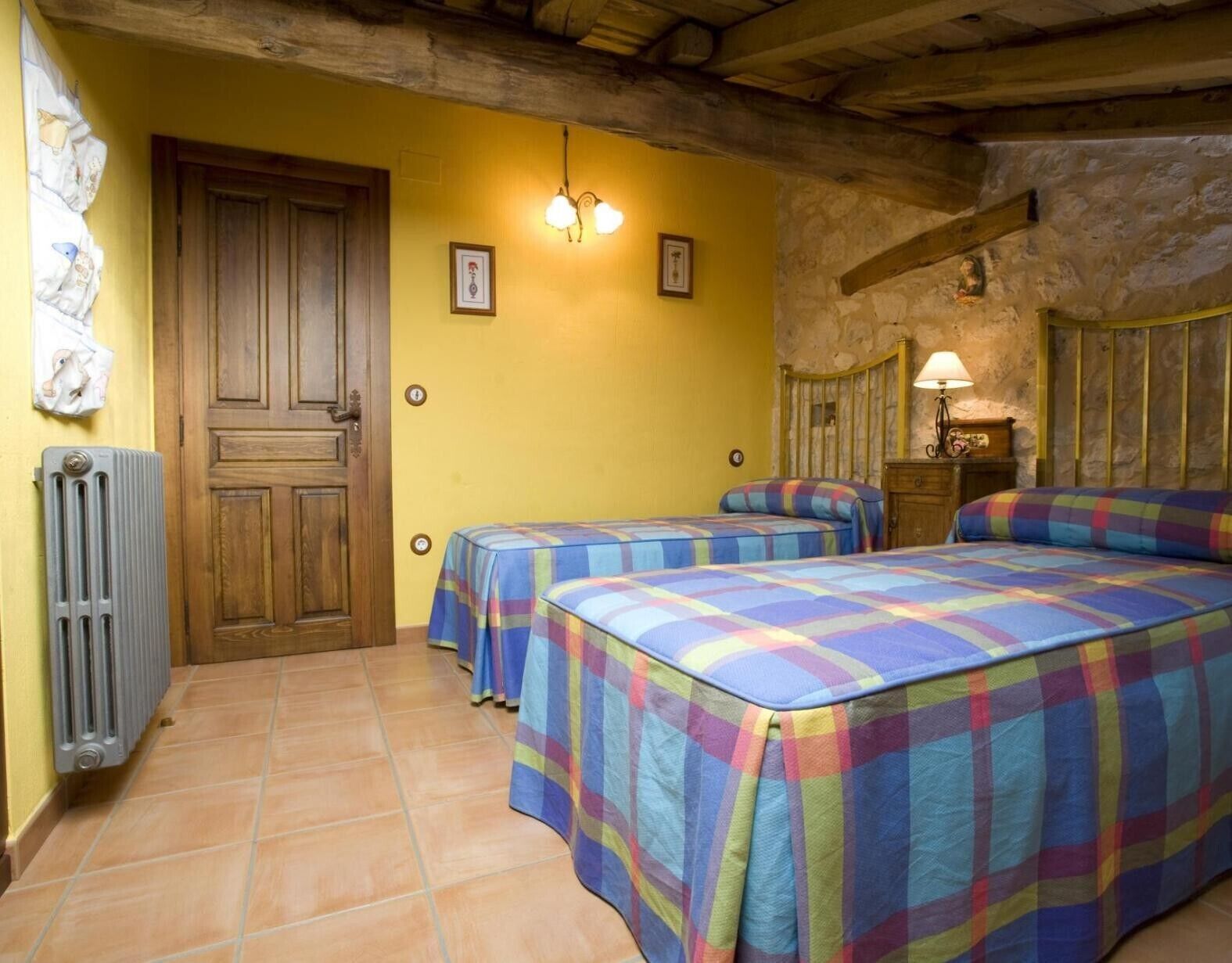 Une chambre avec deux lits, une porte en bois, un radiateur et un mur en pierre.