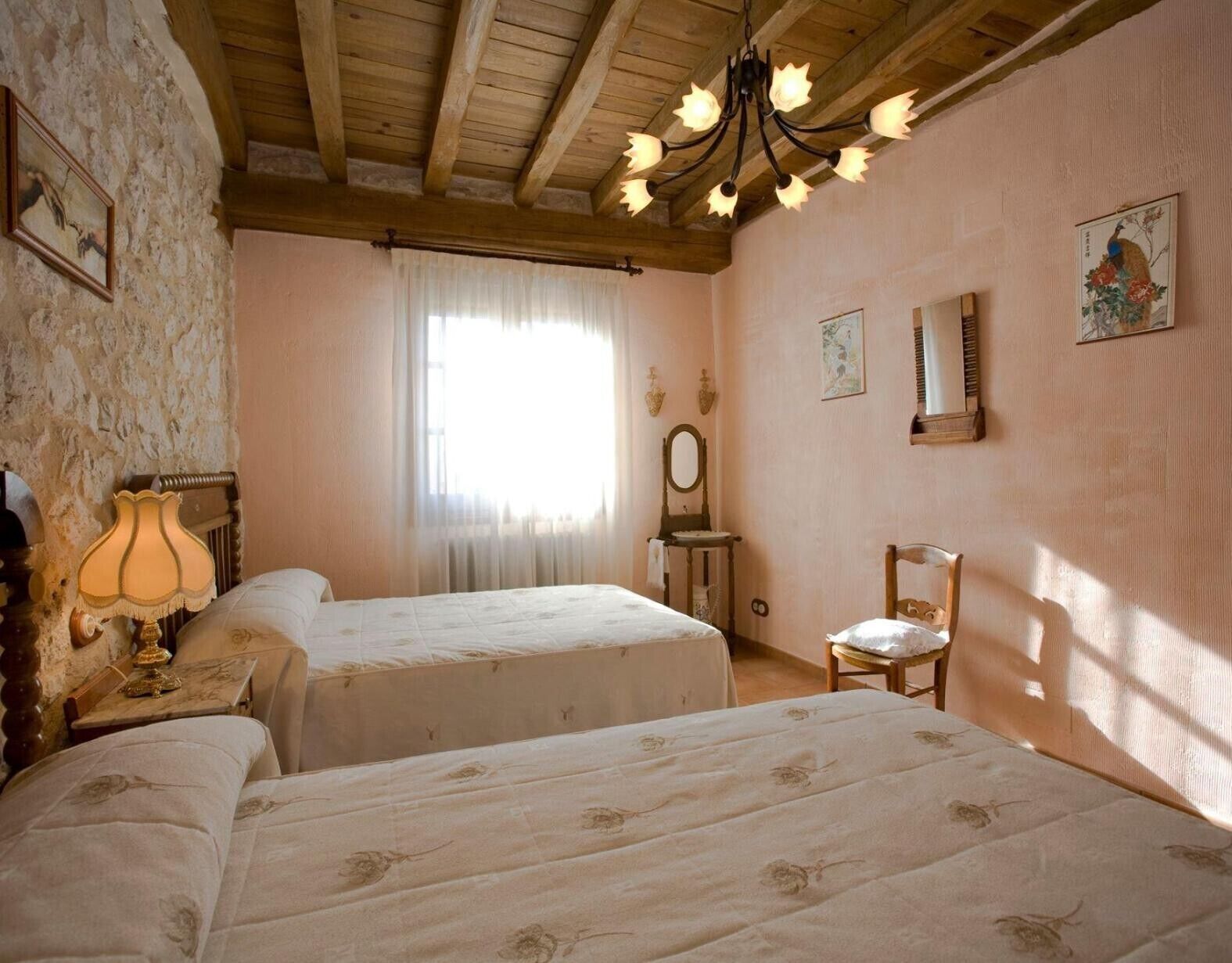 Habitación con dos camas, una araña, un espejo y una ventana con cortinas.