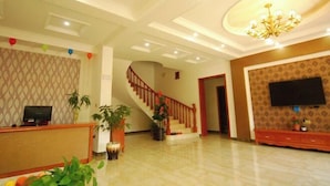 Un hall d’hôtel comprenant un comptoir d’accueil, un escalier, un lustre et un téléviseur à écran plat fixé au mur.