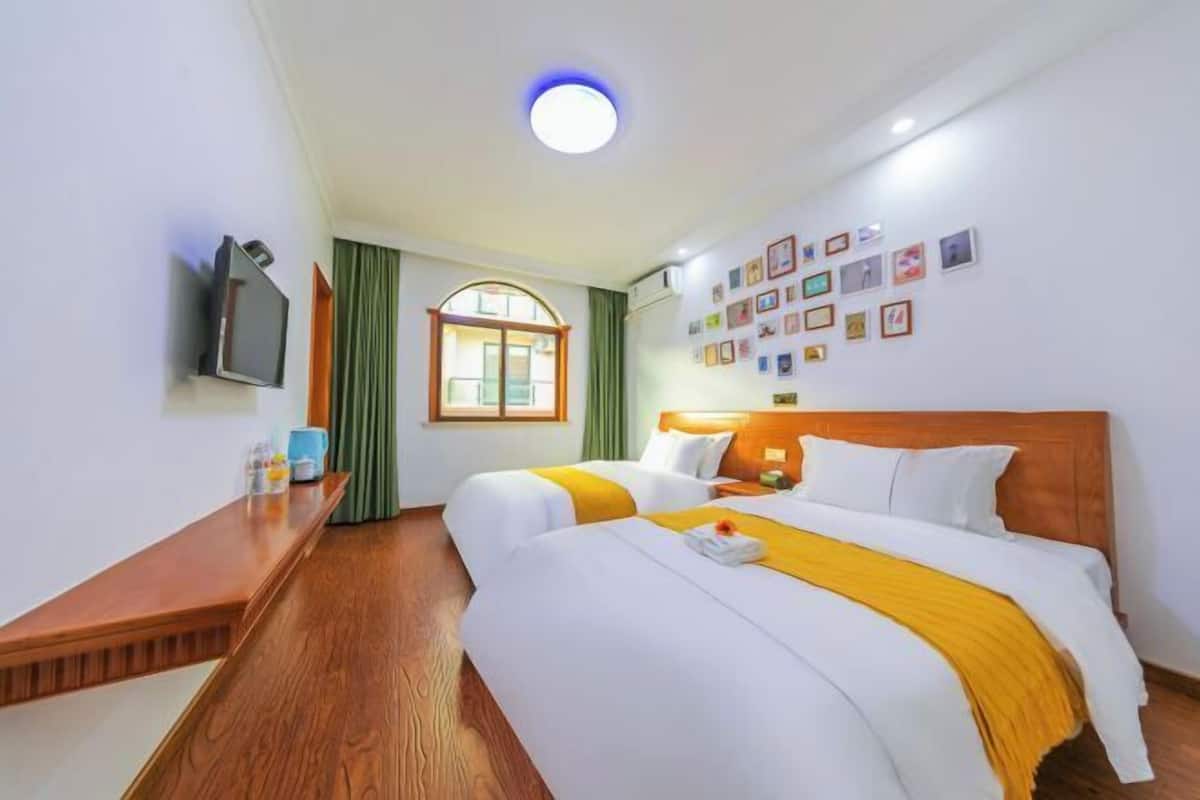 Une chambre d’hôtel avec deux lits, un téléviseur, un bureau en bois, une fenêtre avec des rideaux et un mur orné de tableaux.