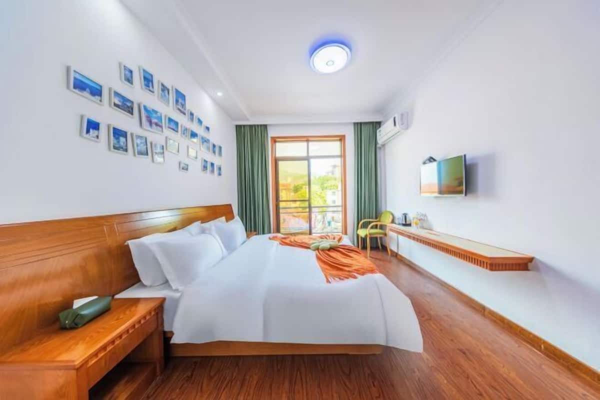 Une chambre d’hôtel avec un grand lit, une table de chevet, une chaise, une télévision et une fenêtre avec des rideaux.