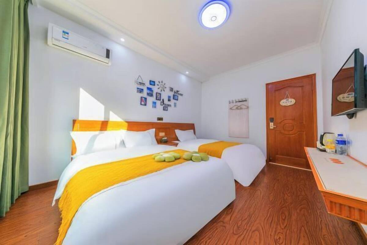 Une chambre d’hôtel avec deux lits, un plancher en bois, un appareil de climatisation, un téléviseur fixé au mur et une porte avec une pancarte.