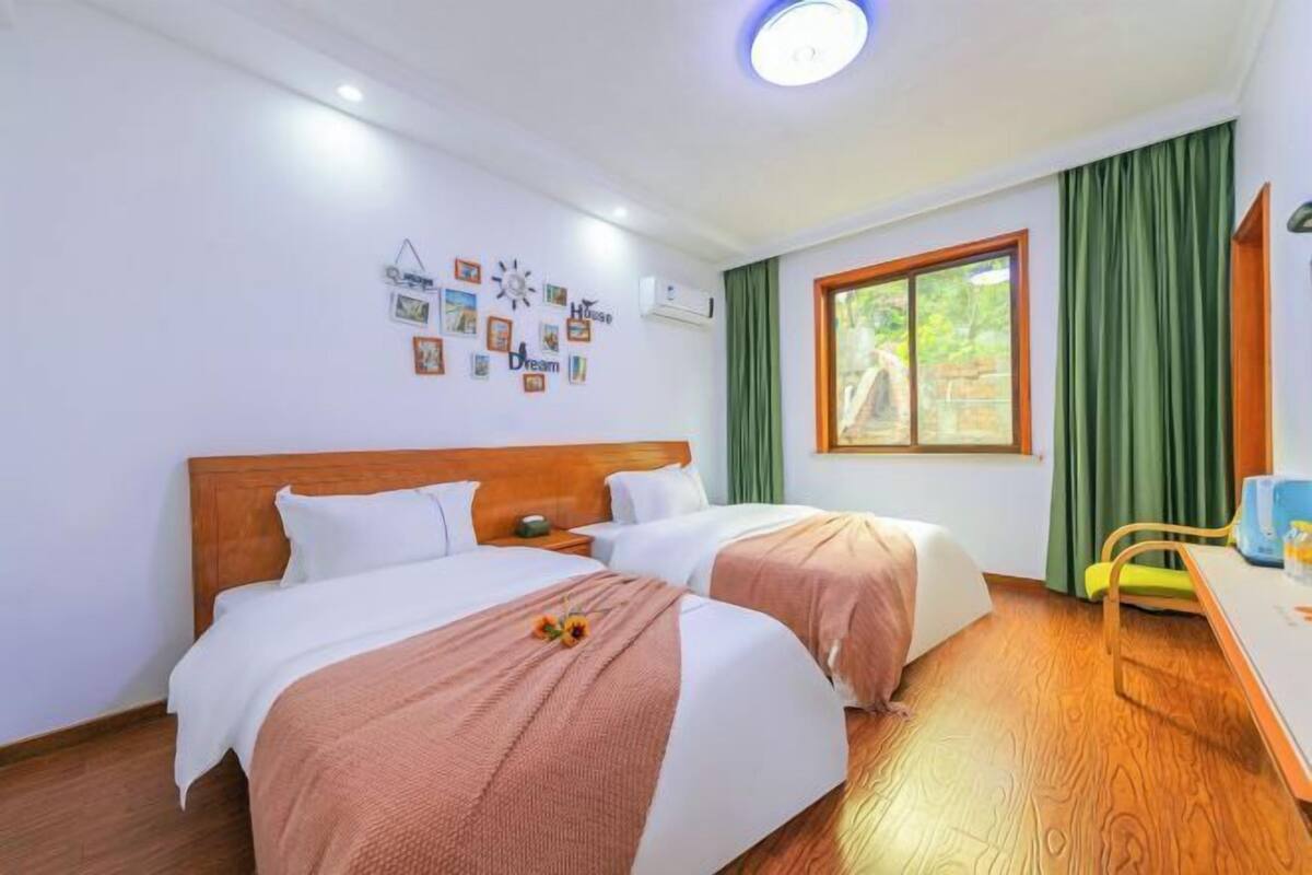 Une chambre d’hôtel avec deux lits, une tête de lit en bois, une fenêtre avec des rideaux, une petite table et des éléments décoratifs sur les murs.