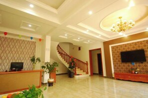 Un hall d’hôtel comprenant un comptoir d’accueil, un escalier, un téléviseur à écran plat fixé au mur et un lustre.