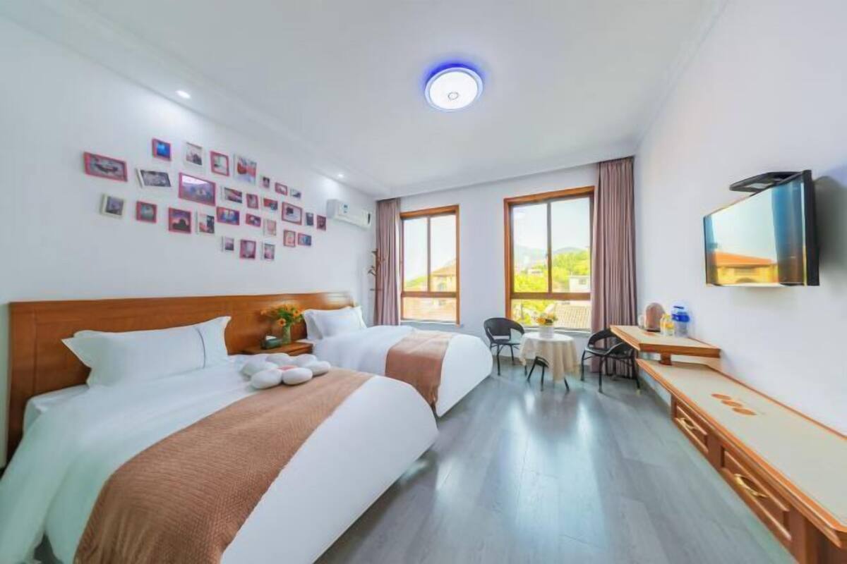 Une chambre d’hôtel avec deux lits, un bureau, une chaise, une télévision et un mur décoré de photos.