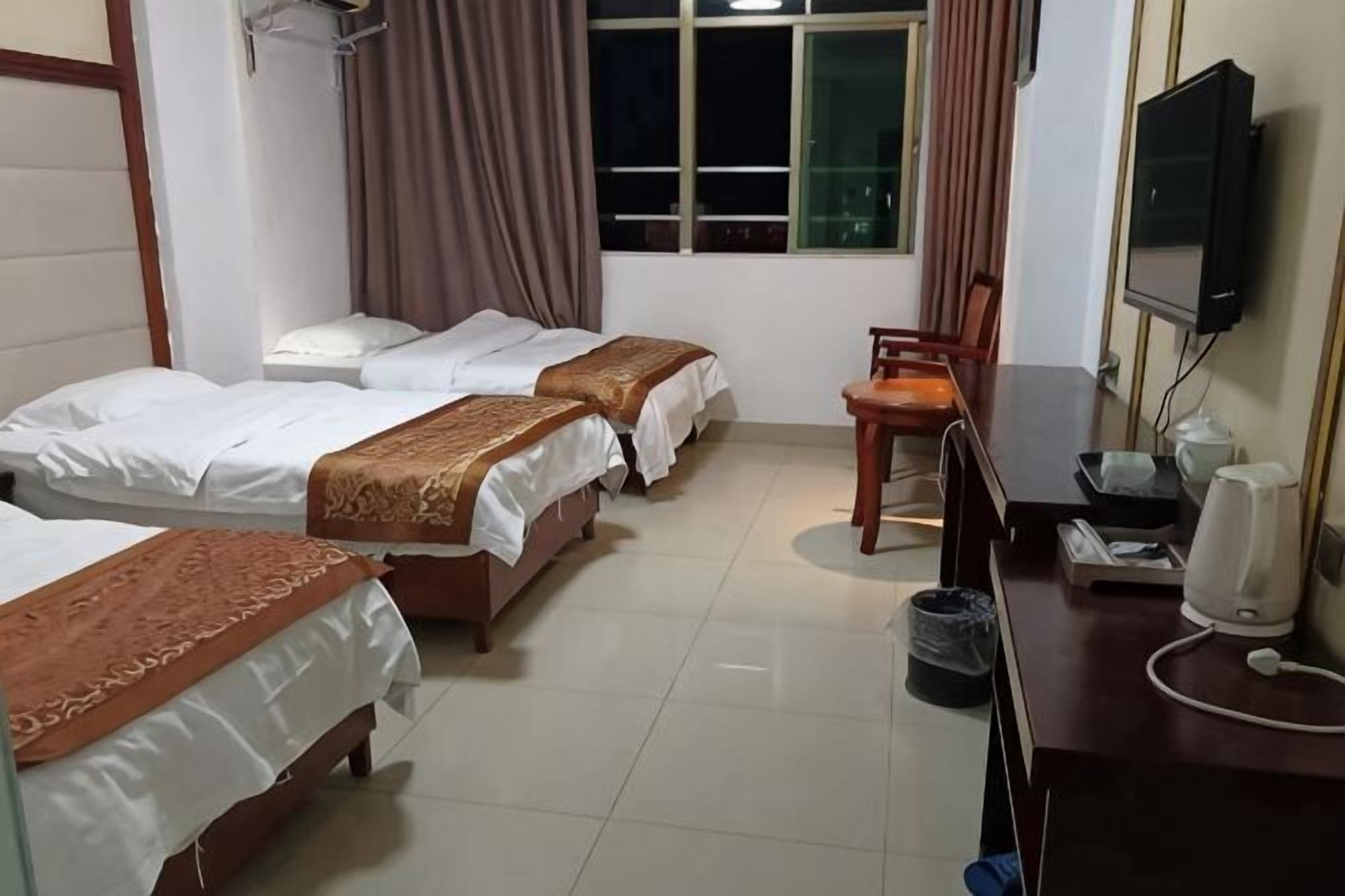 A hotel room with three beds, a desk with a chair, a television, and a window with curtains.