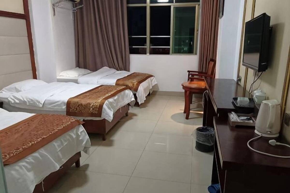 Habitación de hotel con tres camas, un escritorio con una silla, televisor y ventana con cortinas.