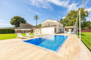 A swimming pool with lounge chairs, a stone building, and a clear sky.