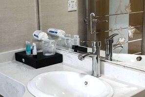 Un baño de hotel con un lavamanos blanco, una bandeja negra con artículos de aseo, un espejo y un perchero para toallas.