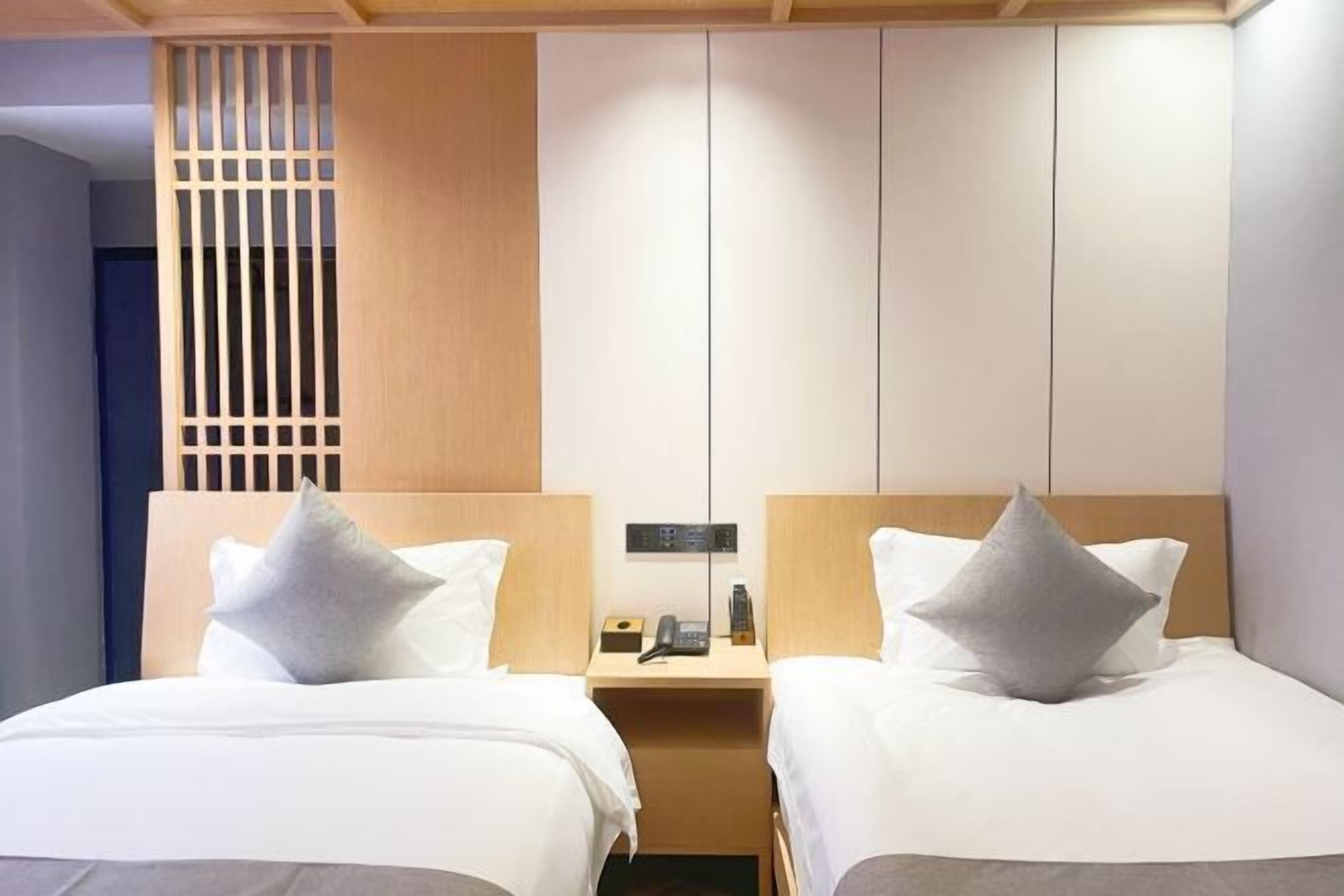 Une chambre d’hôtel avec deux lits, une tête de lit en bois, une table de chevet avec un téléphone et une lampe, et une cloison avec des lattes verticales.