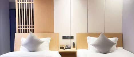 A hotel room with two beds, a wooden headboard, a nightstand with a phone and a lamp, and a partition with vertical slats.