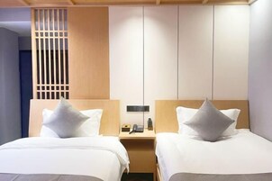 Habitación de hotel con dos camas, cabecera de madera, mesita de noche con teléfono y lámpara, y un separador con listones verticales.