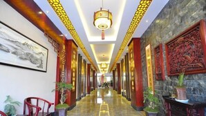 A hotel corridor with a polished marble floor, red chairs, potted plants, and traditional wall art. - Hongcheng Hotel (Luoping)