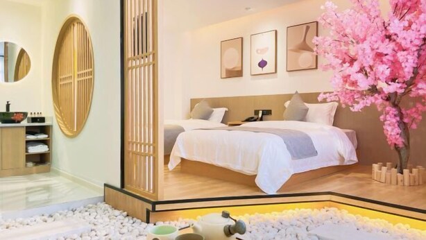 A modern bedroom with a large bed, a wooden partition, and a decorative tree. - Hongcheng Hotel (Luoping)