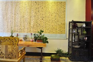 A traditional room with a large wall of calligraphy, a wooden table with a potted plant, and a dark wooden shelf with decorative items. - Hongcheng Hotel (Luoping)