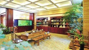 A spacious lobby with a wooden reception desk, a large television screen, and a variety of products on shelves. - Hongcheng Hotel (Luoping)