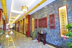 A hotel corridor with a marble floor, traditional wall decorations, and a hanging light fixture. - Hongcheng Hotel (Luoping)