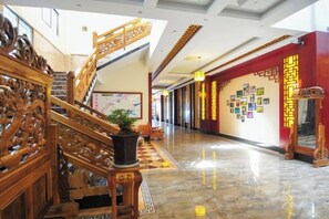 A hotel lobby with a wooden staircase, a checkered floor, and a wall decorated with pictures. - Hongcheng Hotel (Luoping)