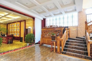 A hotel lobby with a reception desk, a staircase, and a large window.