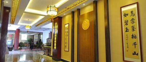 A hotel corridor with a polished floor, framed calligraphy on the walls, and a hanging light fixture.