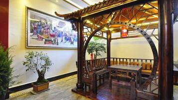 A traditional wooden pavilion with seating, a framed artwork on the wall, and a potted plant.