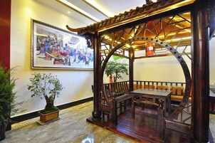 A traditional wooden pavilion with seating, a framed artwork on the wall, and a potted plant.